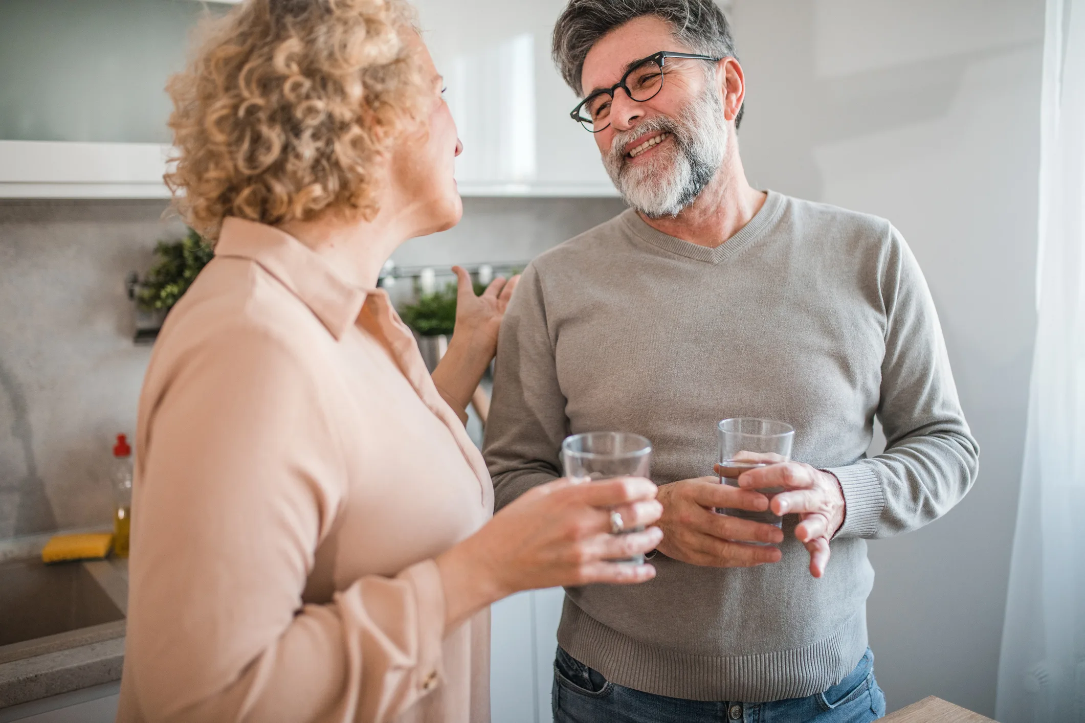 Loving couple standing at the kitchen counter, refreshing themselves by drinking water and bonding